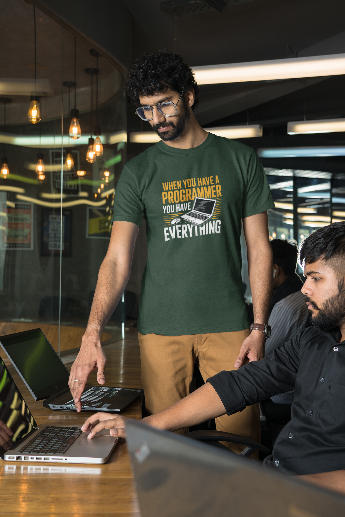 Two men working on laptops in a modern office setting with one wearing a green t-shirt.