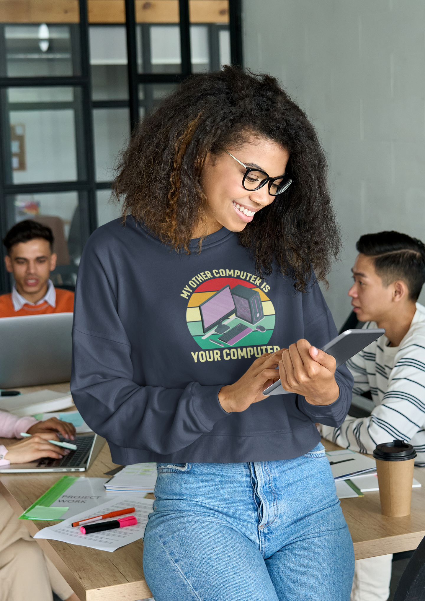 Woman wearing a sweatshirt with a graphic design, sitting at a desk in an office setting.