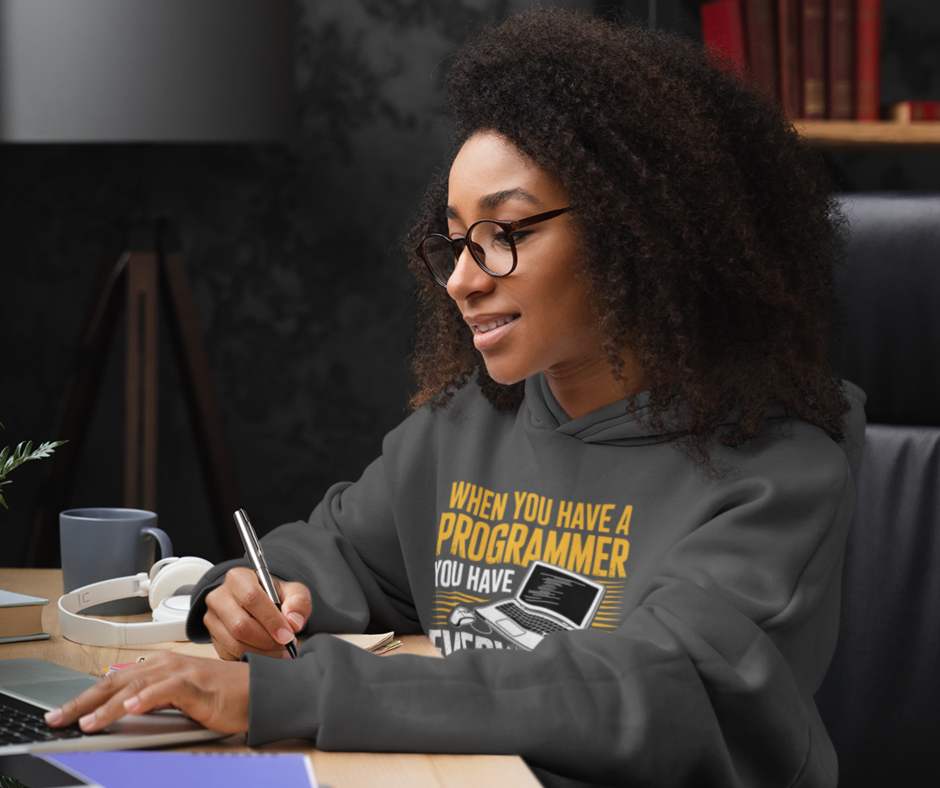 Person wearing a hoodie with text, sitting at a desk with a laptop.