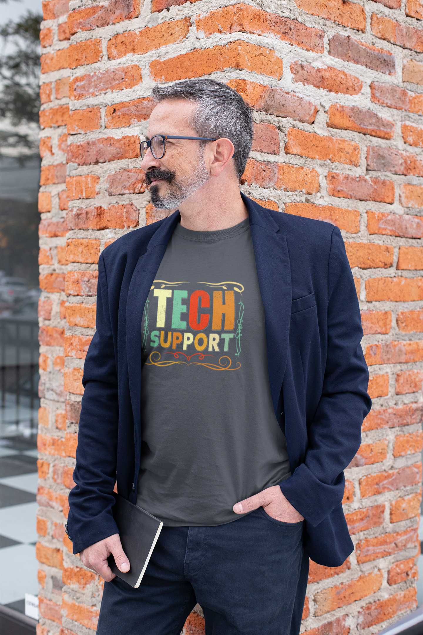 Man wearing a 'Tech Support' t-shirt standing against a brick wall.